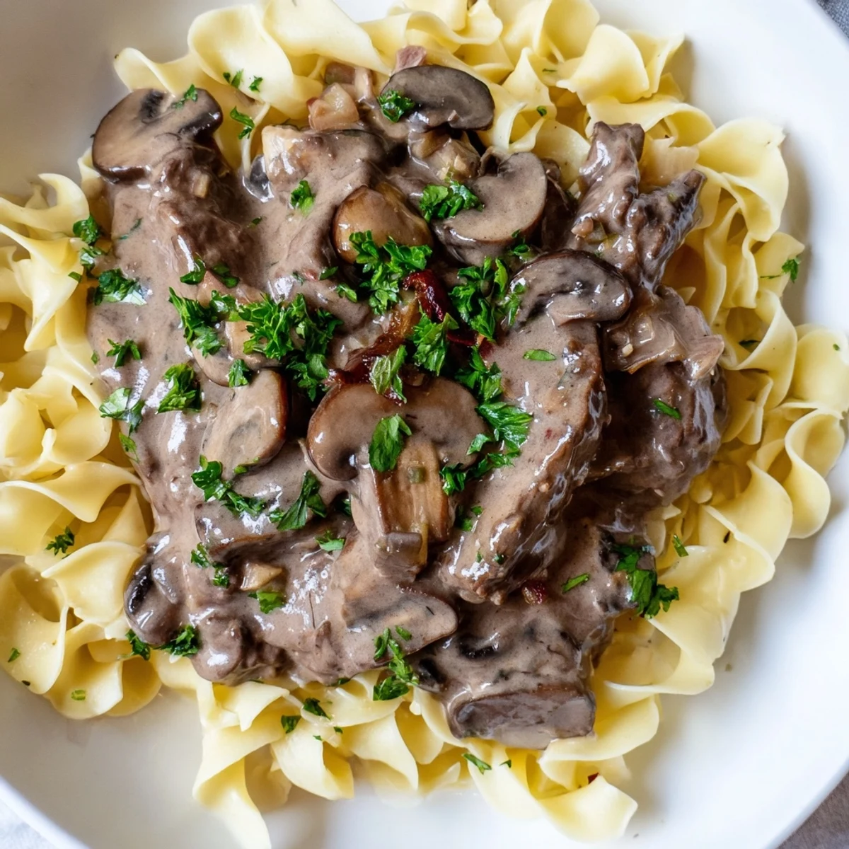 Savory Beef Stroganoff over Egg Noodles with Mushroom Sauce ready to eat. The tender beef and sautéed onions are nestled in a rich, creamy mushroom gravy over buttery noodles. A perfect weeknight comfort meal for four.