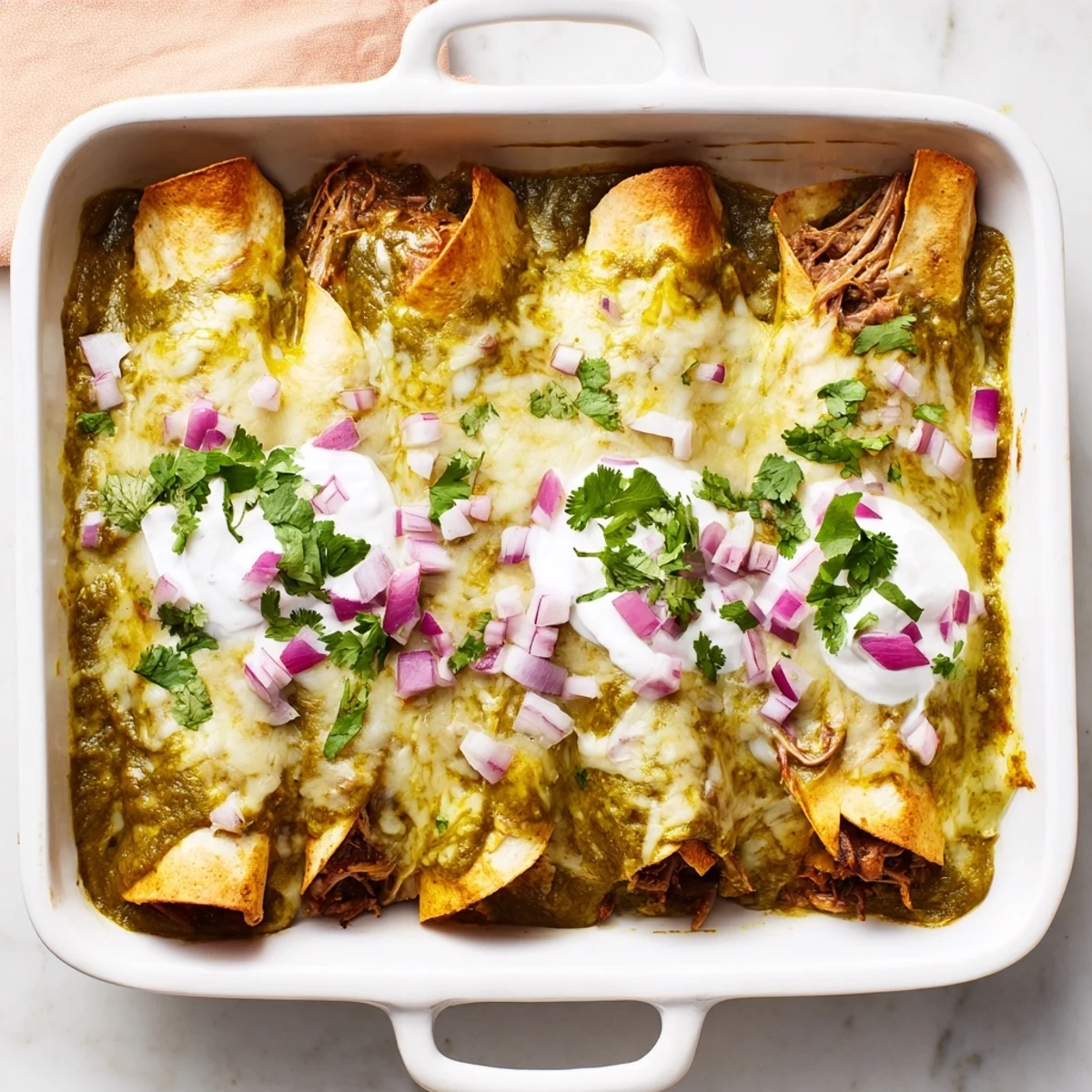 Tender shredded beef filling inside soft corn tortillas, smothered in vibrant green tomatillo sauce and melted Monterey Jack cheese, garnished with fresh cilantro and sour cream.