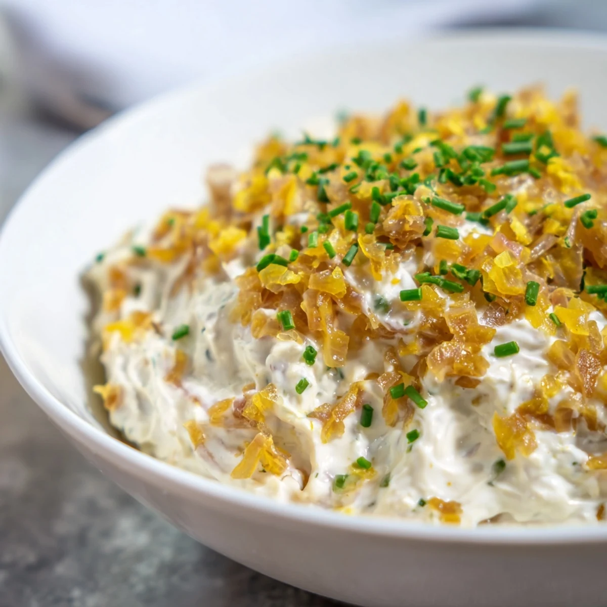 A bowl of creamy Game Day Onion Dip studded with golden caramelized onions, surrounded by crunchy potato chips for dipping.