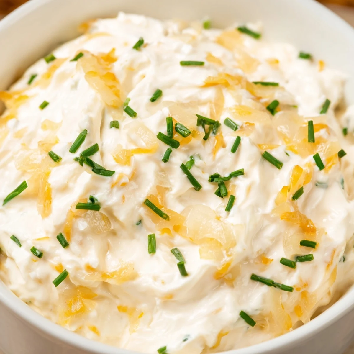 A close-up of rich Game Day Onion Dip garnished with fresh chives, served alongside a platter of crisp kettle chips.