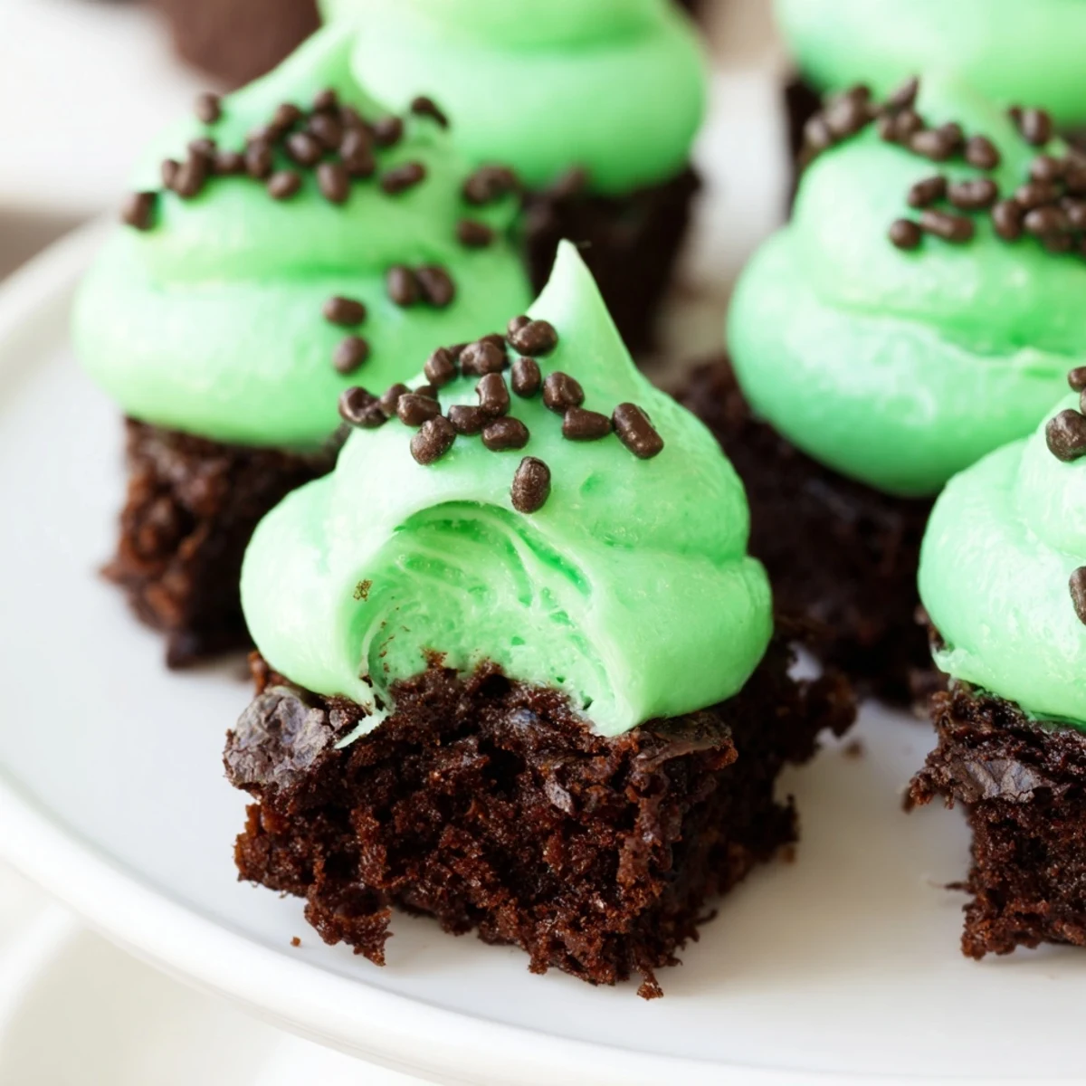 Four St. Patricks Day Mint Brownie Bites with minty frosting and chocolate sprinkles on a wooden board.