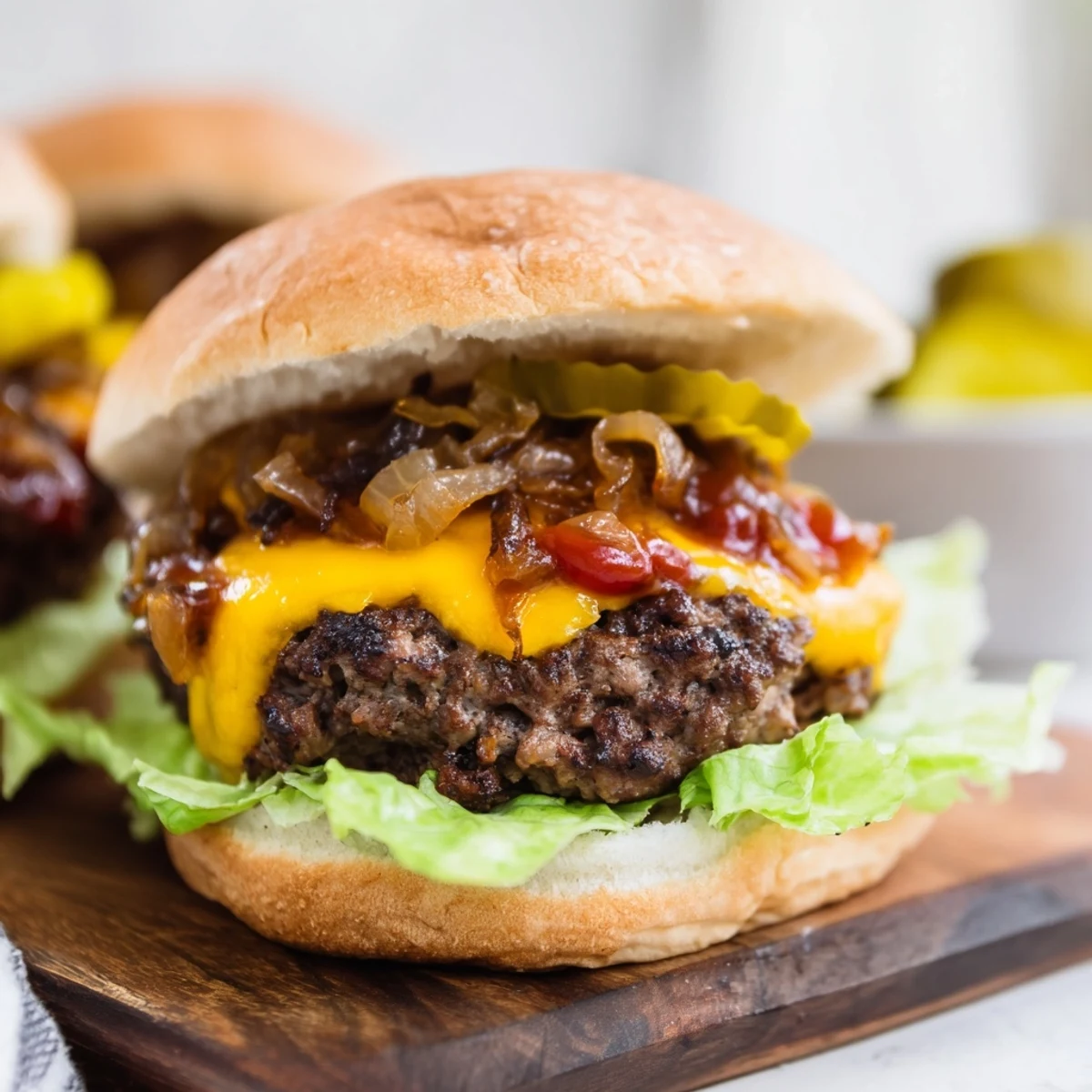 Classic Beef Burgers with Caramelized Onions garnished with pickles and tomatoes on a rustic wooden serving board.