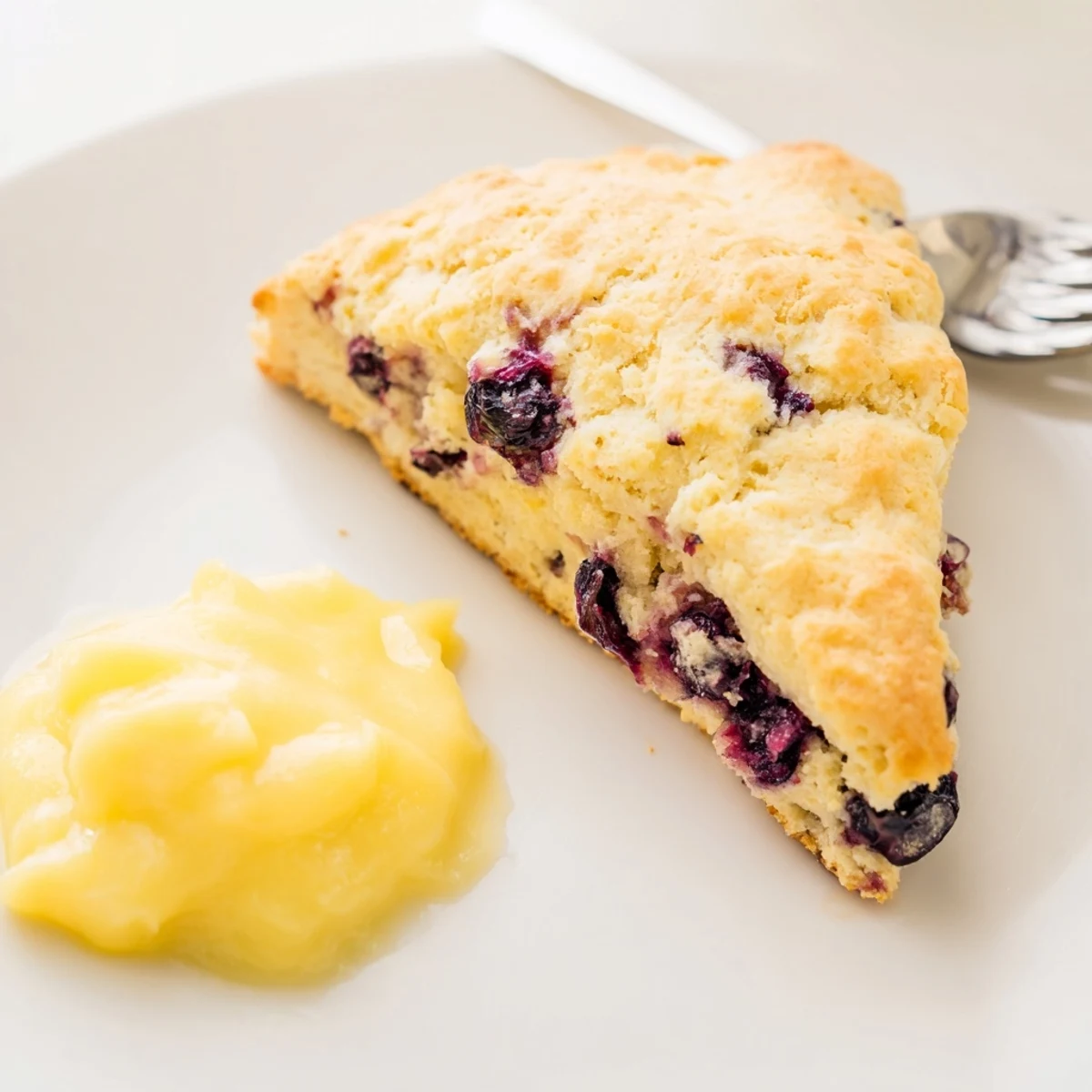 Golden-brown Lemon Blueberry Scones with Lemon Curd stacked on a rustic wooden board, showcasing juicy blueberries and a zesty lemon glaze.
