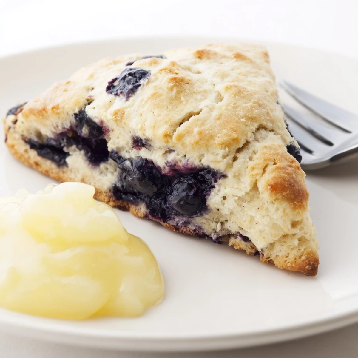 Freshly baked Lemon Blueberry Scones with Lemon Curd, featuring crumbly textures and a vibrant yellow drizzle, perfect for a cozy breakfast spread.