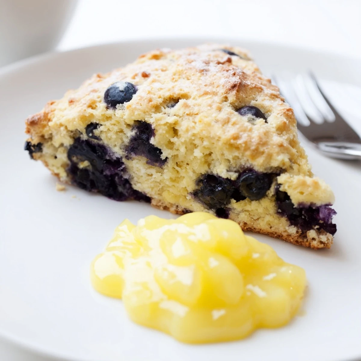 A close-up of warm Lemon Blueberry Scones with Lemon Curd, revealing tender interiors bursting with blueberries and a side of tangy lemon sauce.