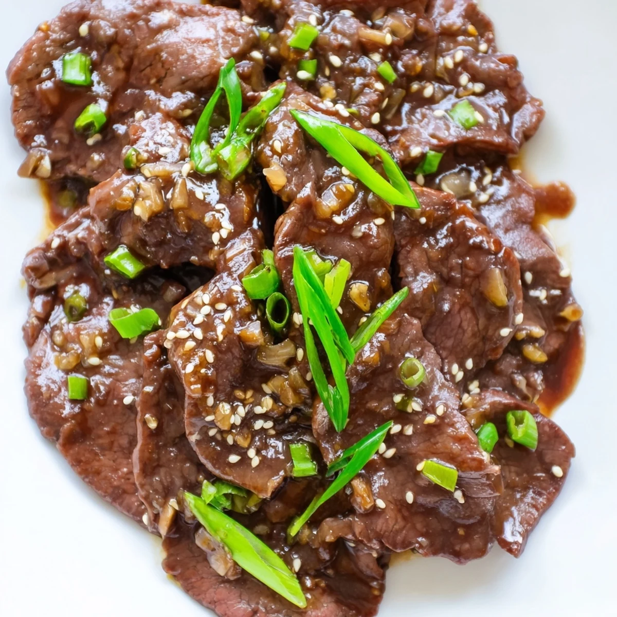 Close-up of Ultimate Slow Cooker Mongolian Beef glistening with savory-sweet sauce and topped with sesame seeds and scallions.
