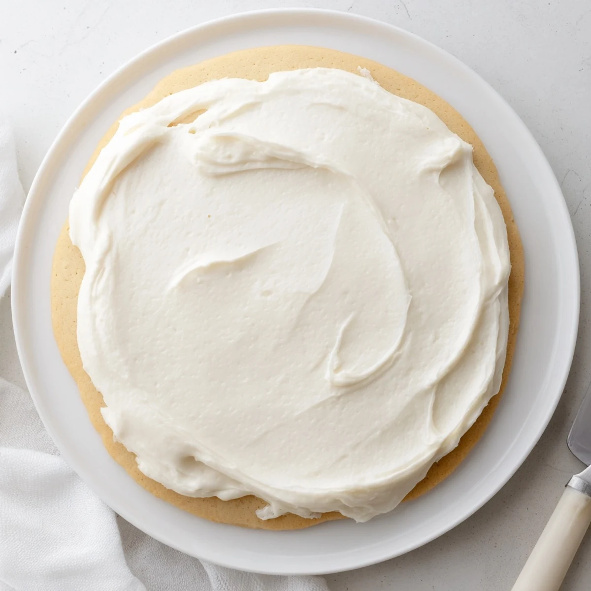 Easy Sugar Cookie Frosting in a mixing bowl beside freshly frosted cookies on a tray.