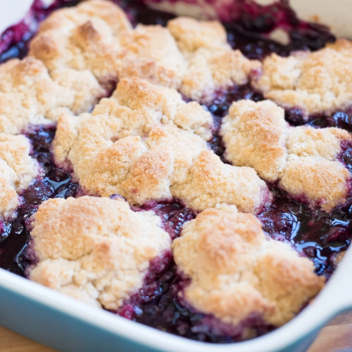 Rustic blueberry cobbler with frozen berries served in a dish, berry filling peeking through tender topping.