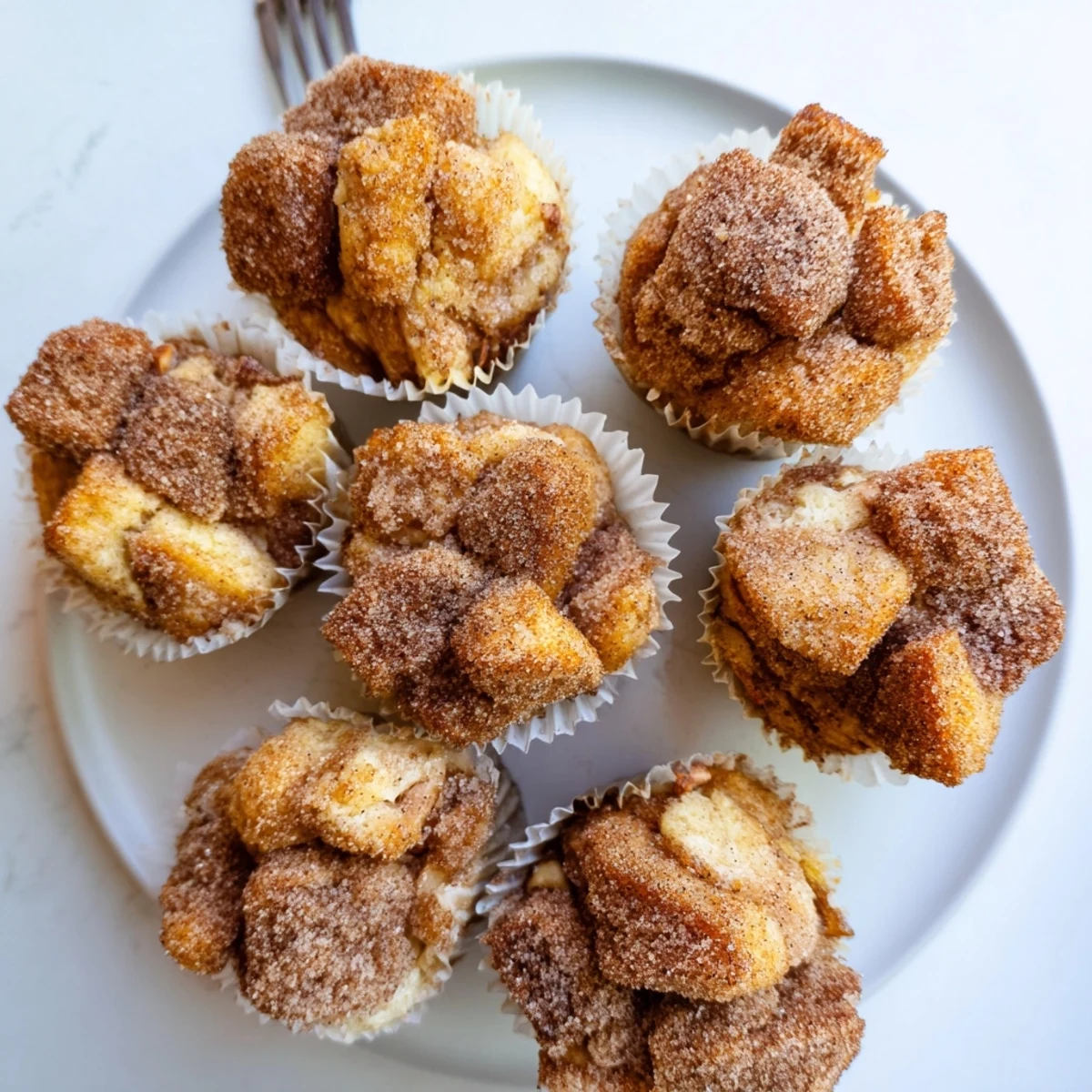 Golden-brown Cinnamon Sugar French Toast Muffins sit on a wooden board, glistening with a sweet glaze.