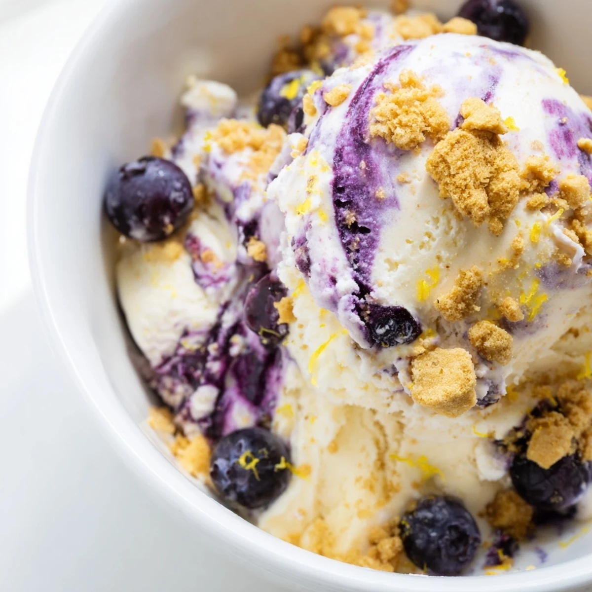 Churned Lemon Blueberry Cheesecake Ice Cream in a loaf pan, showing graham cracker crumbs and a zesty citrus aroma.