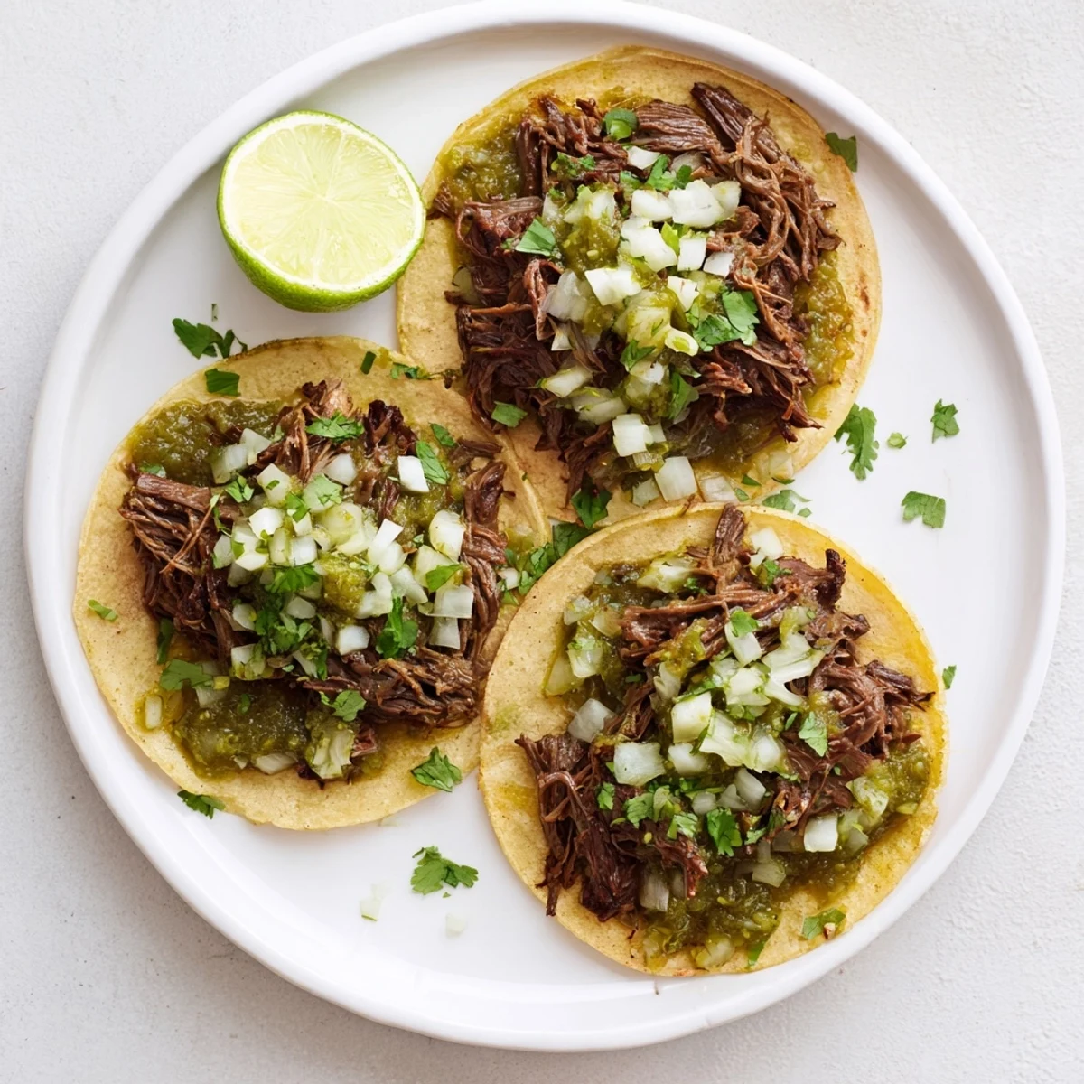Close-up of tender, slow-braised Beef Cheek Tacos garnished with zesty salsa verde and lime wedges on a rustic wooden serving board.