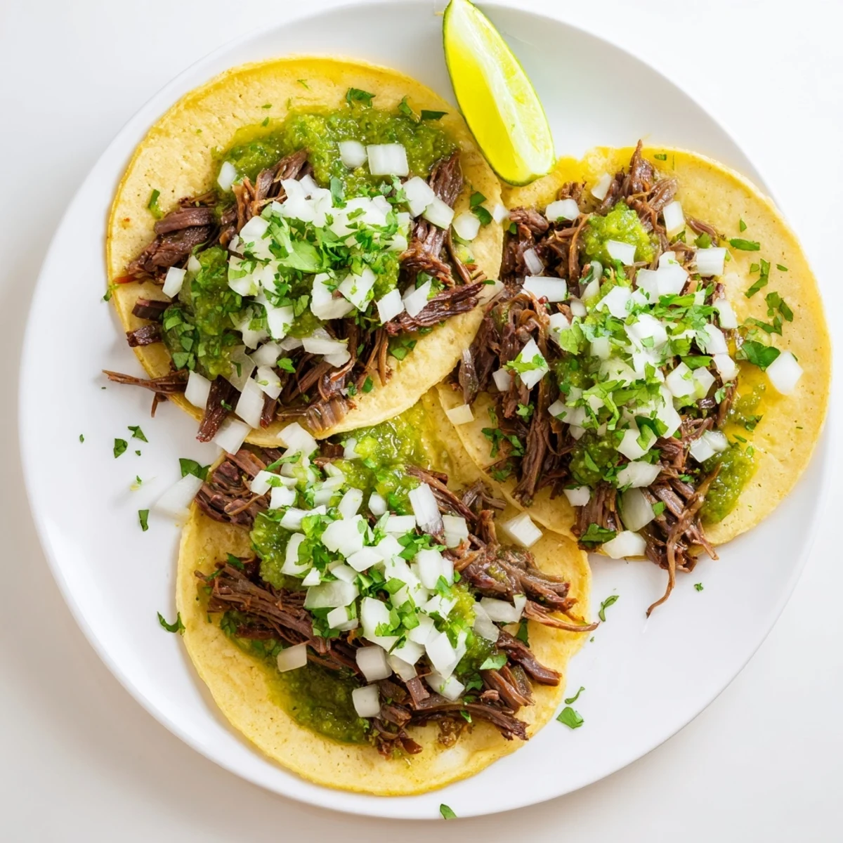 Delicious Mexican-style Beef Cheek Tacos with succulent shredded beef, fresh cilantro, and a drizzle of sauce on a white plate.