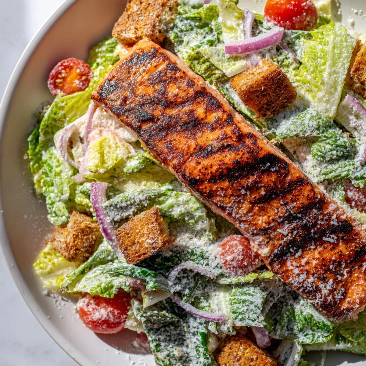 Vibrant plate featuring seasoned grilled salmon over crunchy Caesar salad with red onion and toasted croutons