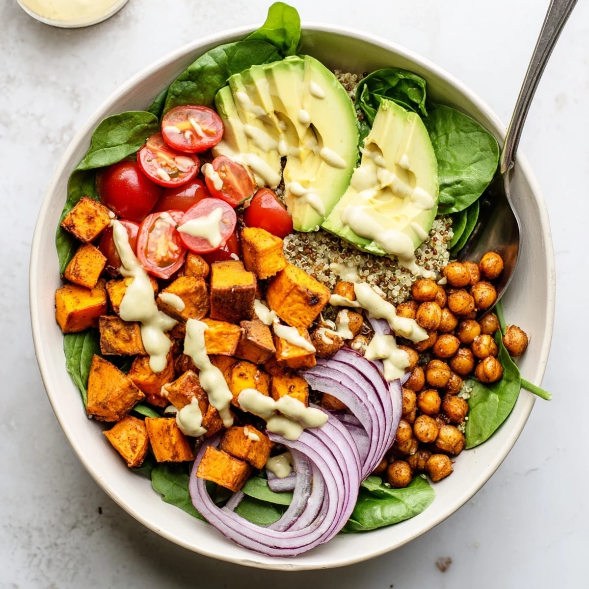 Vibrant hearty sweet potato bowl layered with spinach, cherry tomatoes, and creamy dressing