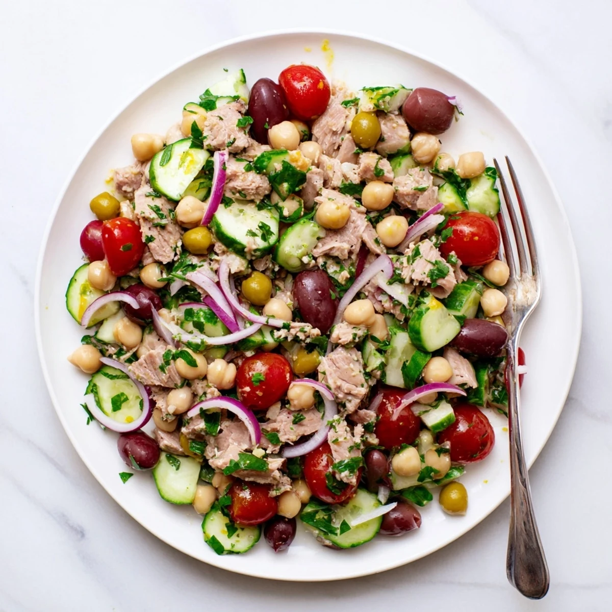 Mediterranean-style hearty tuna and garbanzo bean salad featuring cherry tomatoes, olives, and fresh herbs on white platter