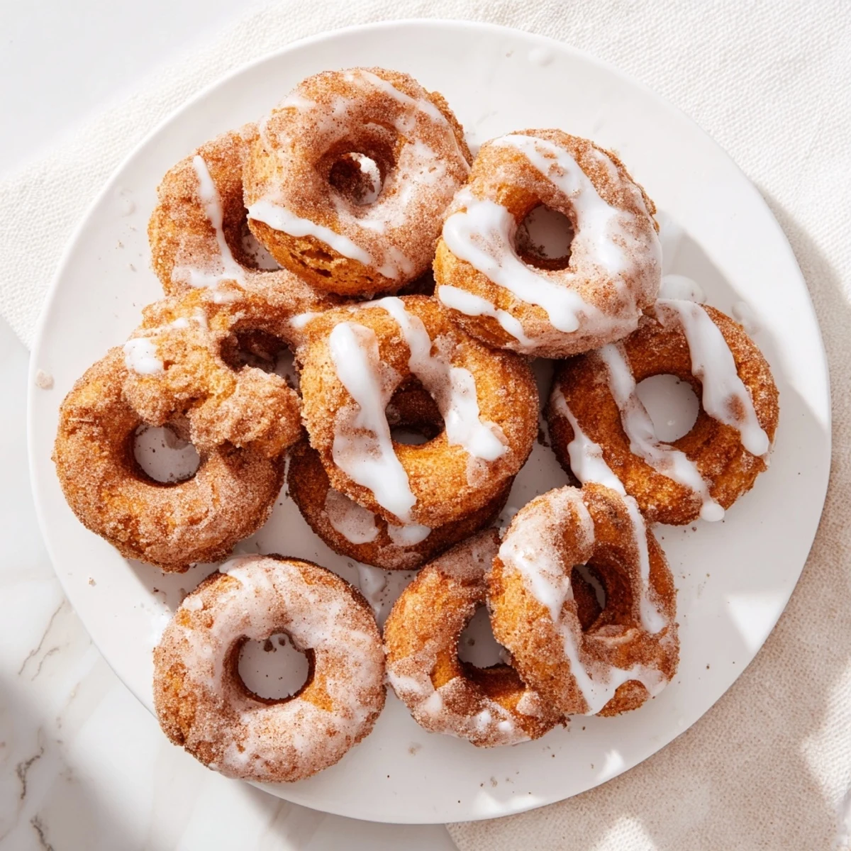 Soft glazed pumpkin donuts arranged on a rustic wooden board with autumn leaves scattered nearby