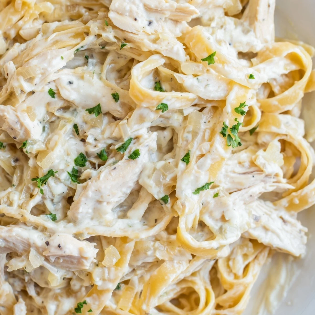 Golden brown Chicken Alfredo pasta dish garnished with fresh parsley and parmesan cheese on a rustic wooden table