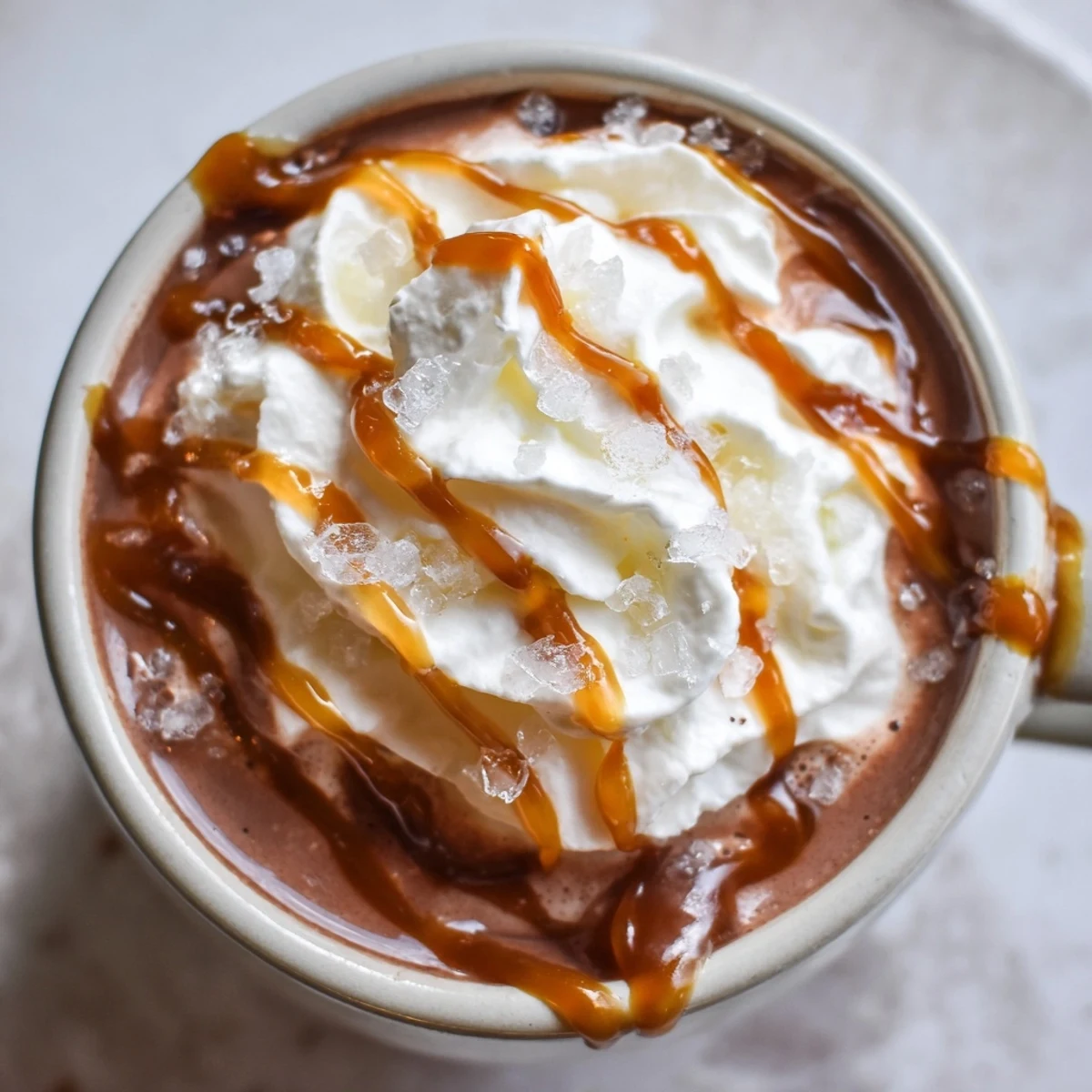 Decadent salted caramel hot chocolate garnished with flaky sea salt and extra caramel sauce