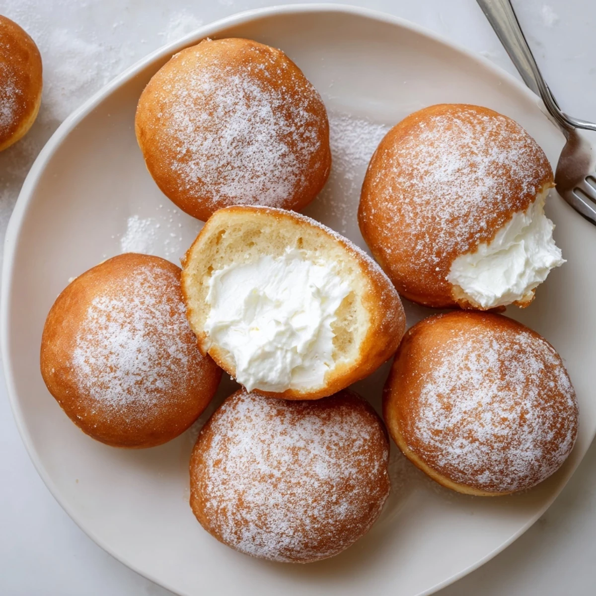 Golden fried Korean Milk Cream Donuts dusted with powdered sugar on a white plate