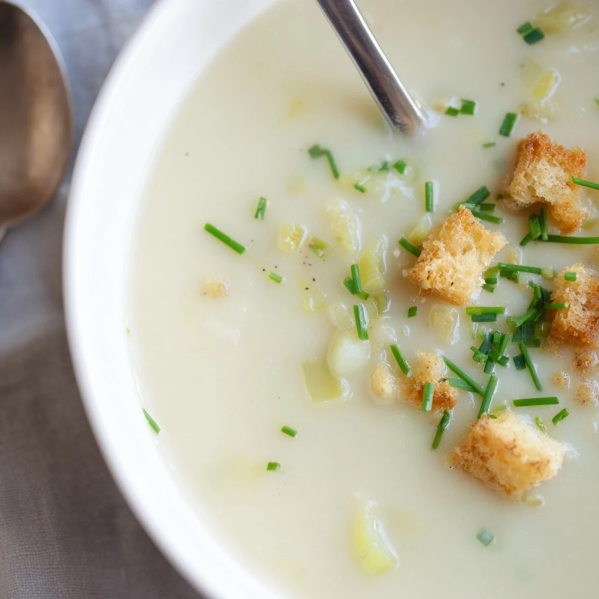 Golden potato leek soup steaming in rustic crock with crusty bread slice on wooden board