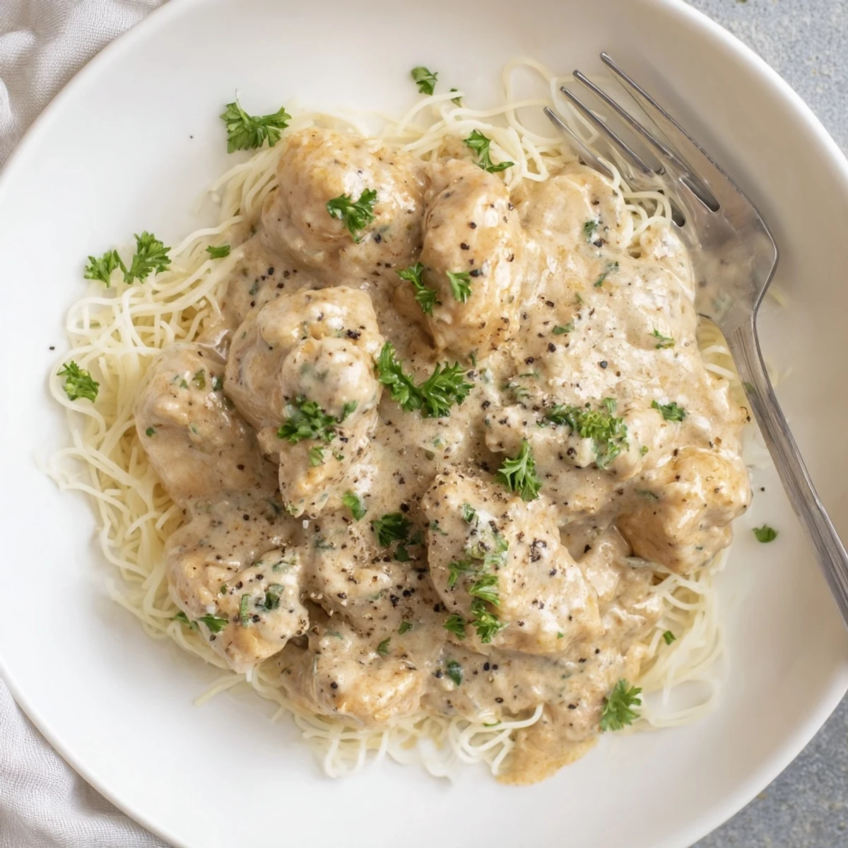 Crock Pot Angel Chicken served over angel hair pasta with creamy golden sauce and fresh parsley garnish