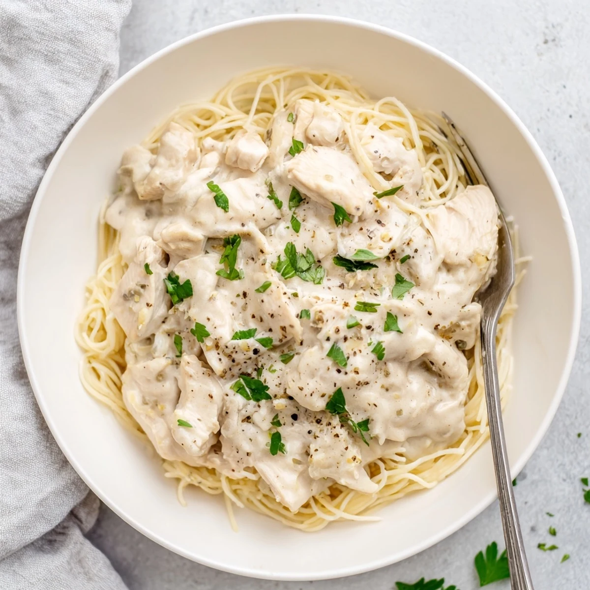Tender slow-cooked chicken breasts in rich cream cheese sauce atop a bed of fluffy angel hair pasta