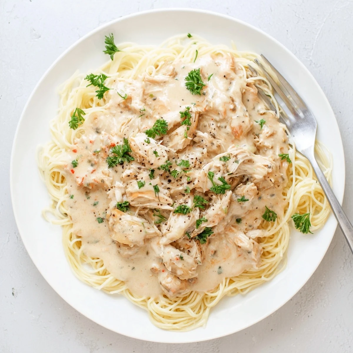 Creamy Crock Pot Angel Chicken dish with shredded chicken draped over pasta and topped with black pepper