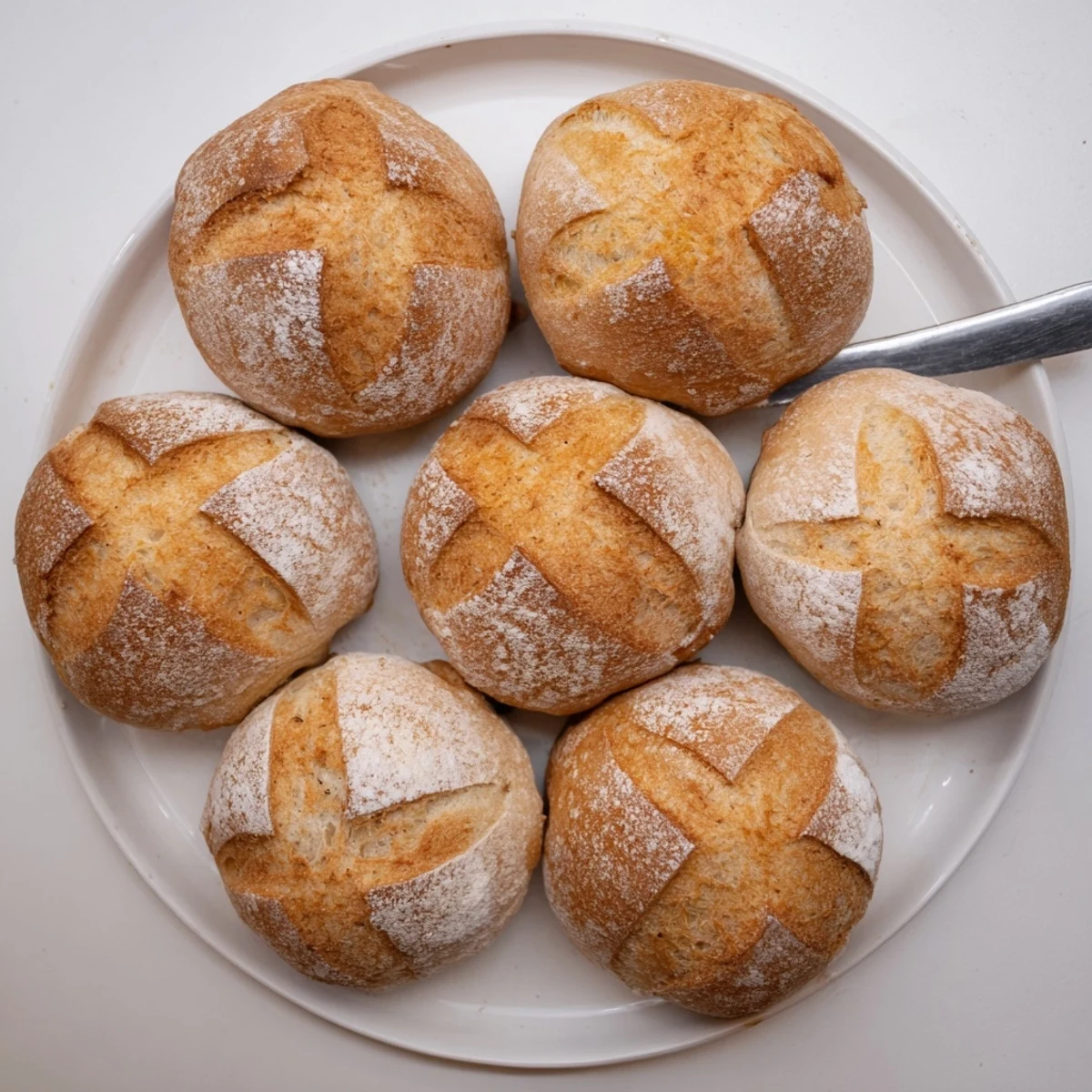 Eight homemade crusty French bread rolls arranged on parchment ready for baking