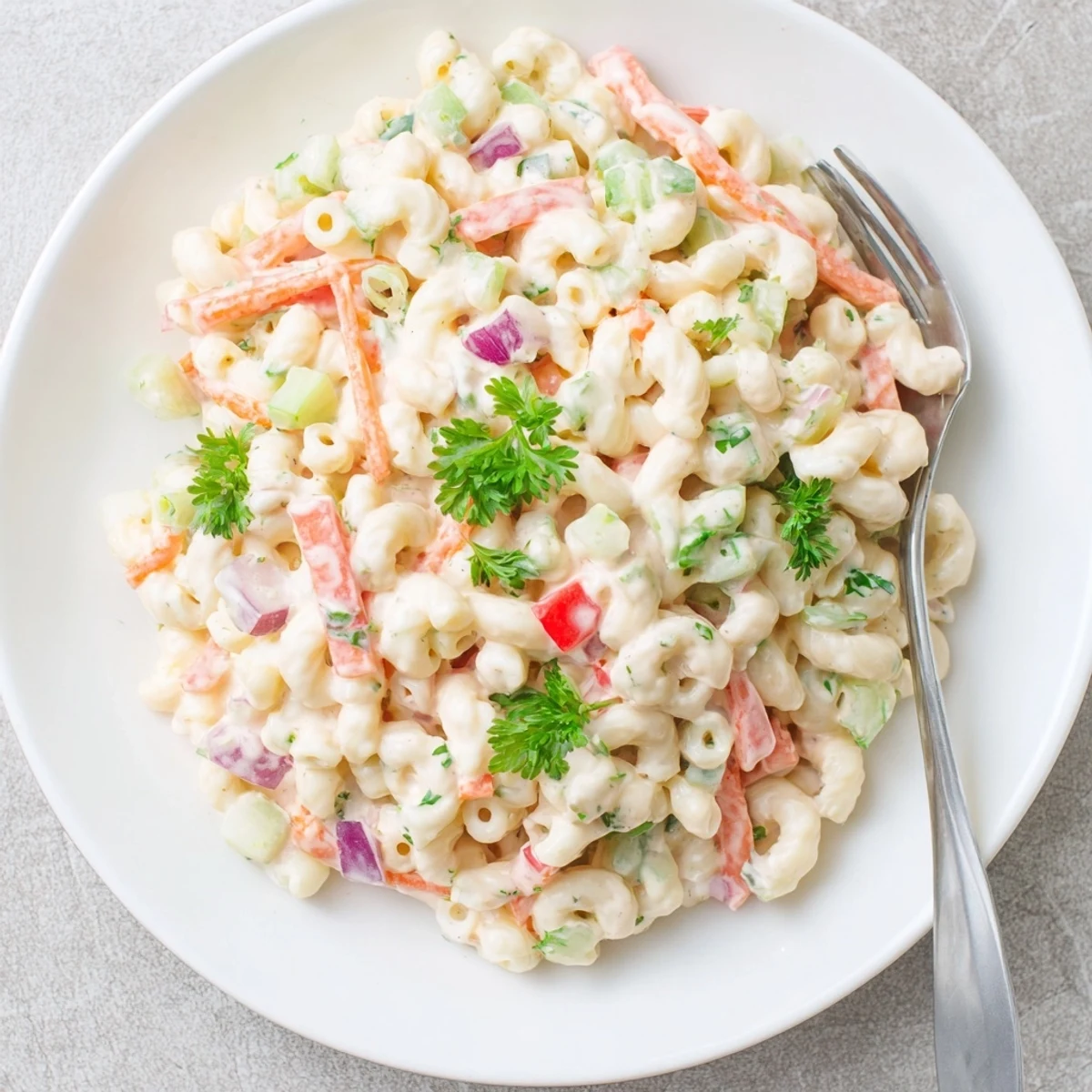 Creamy tangy macaroni salad with colorful diced vegetables in a white serving bowl