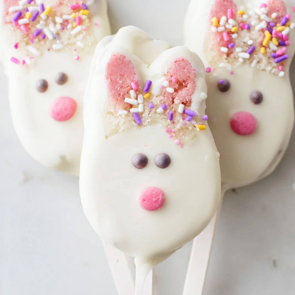 Creamy white chocolate bunny cakesicles decorated with pink ears and festive sprinkles