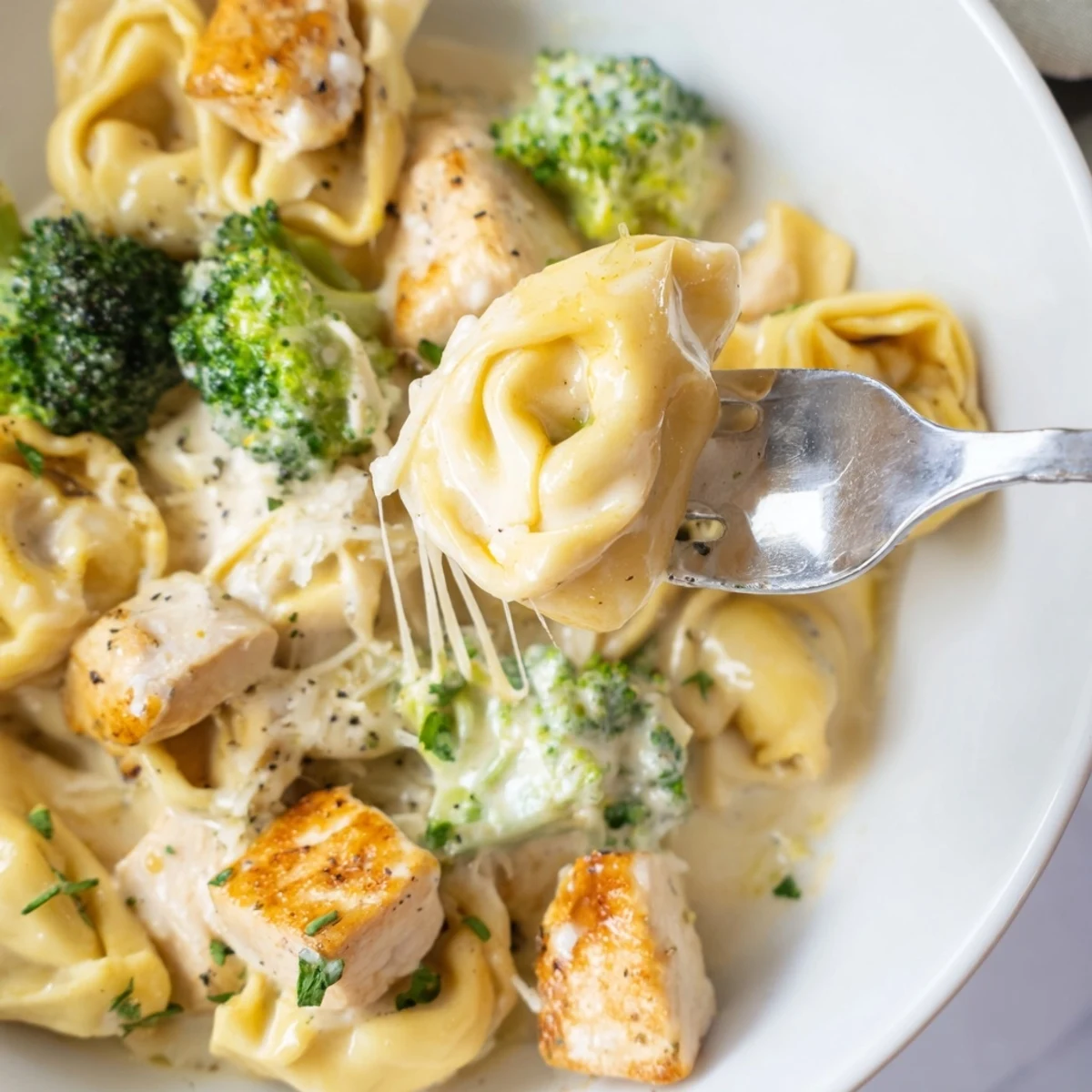 Steaming plate of Creamy Garlic Parmesan Tortellini Chicken Broccoli Recipe, garnished with parsley