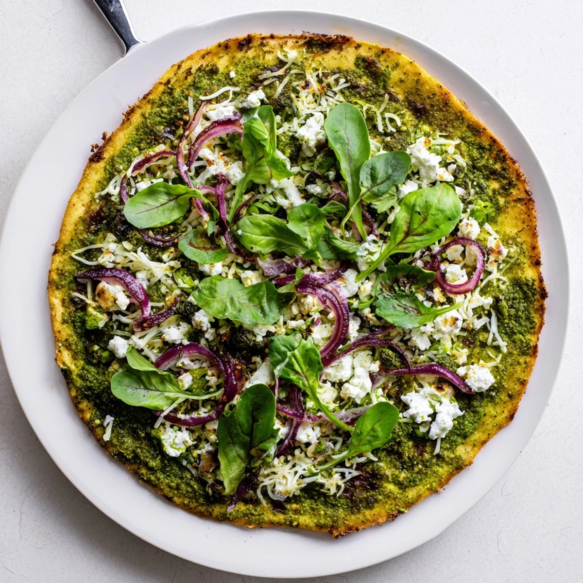 Slice of broccoli pesto pizza featuring creamy feta, baby spinach, and red onion on crispy baked dough