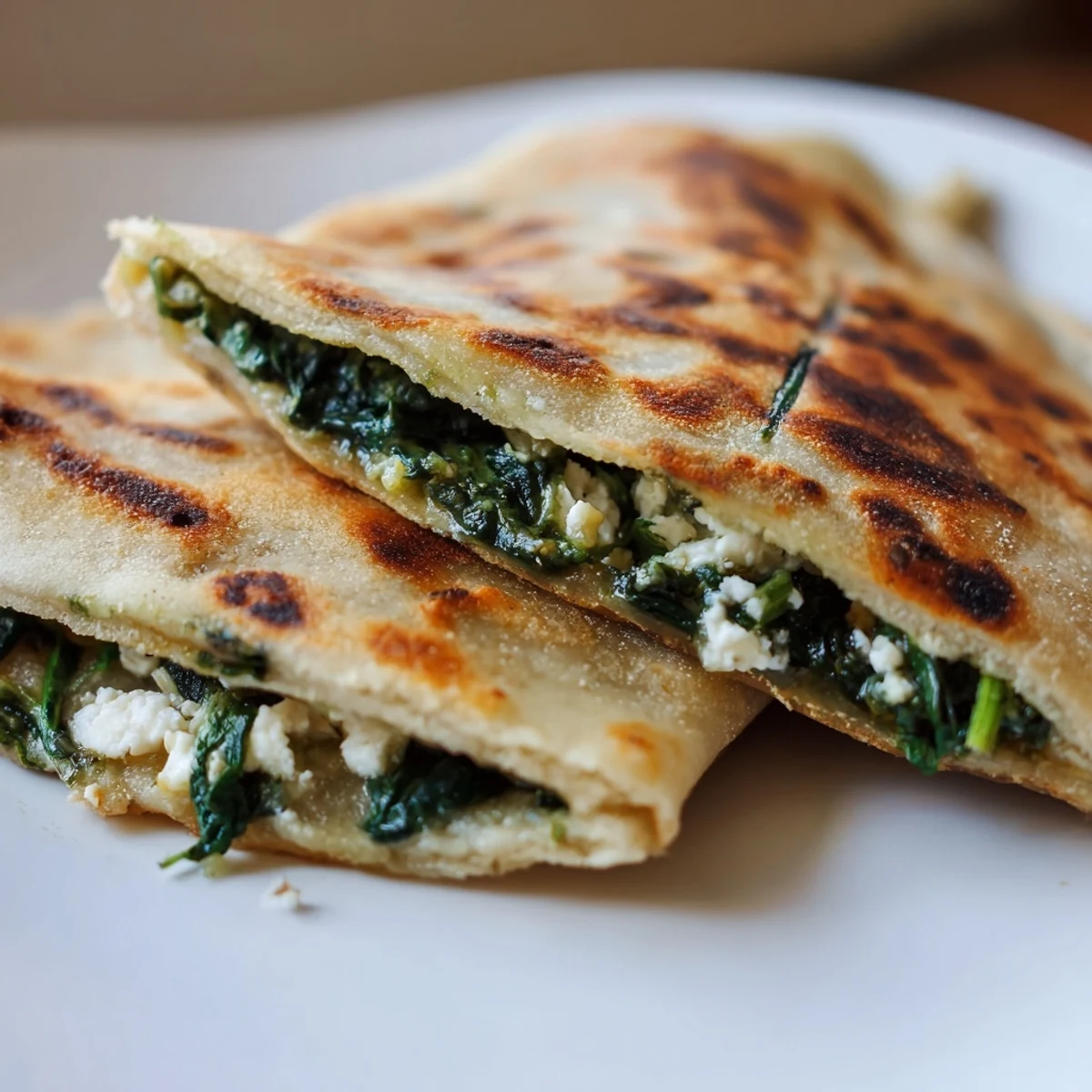 Golden brown Turkish gozleme stuffed with fresh spinach and crumbled feta cheese on a wooden board