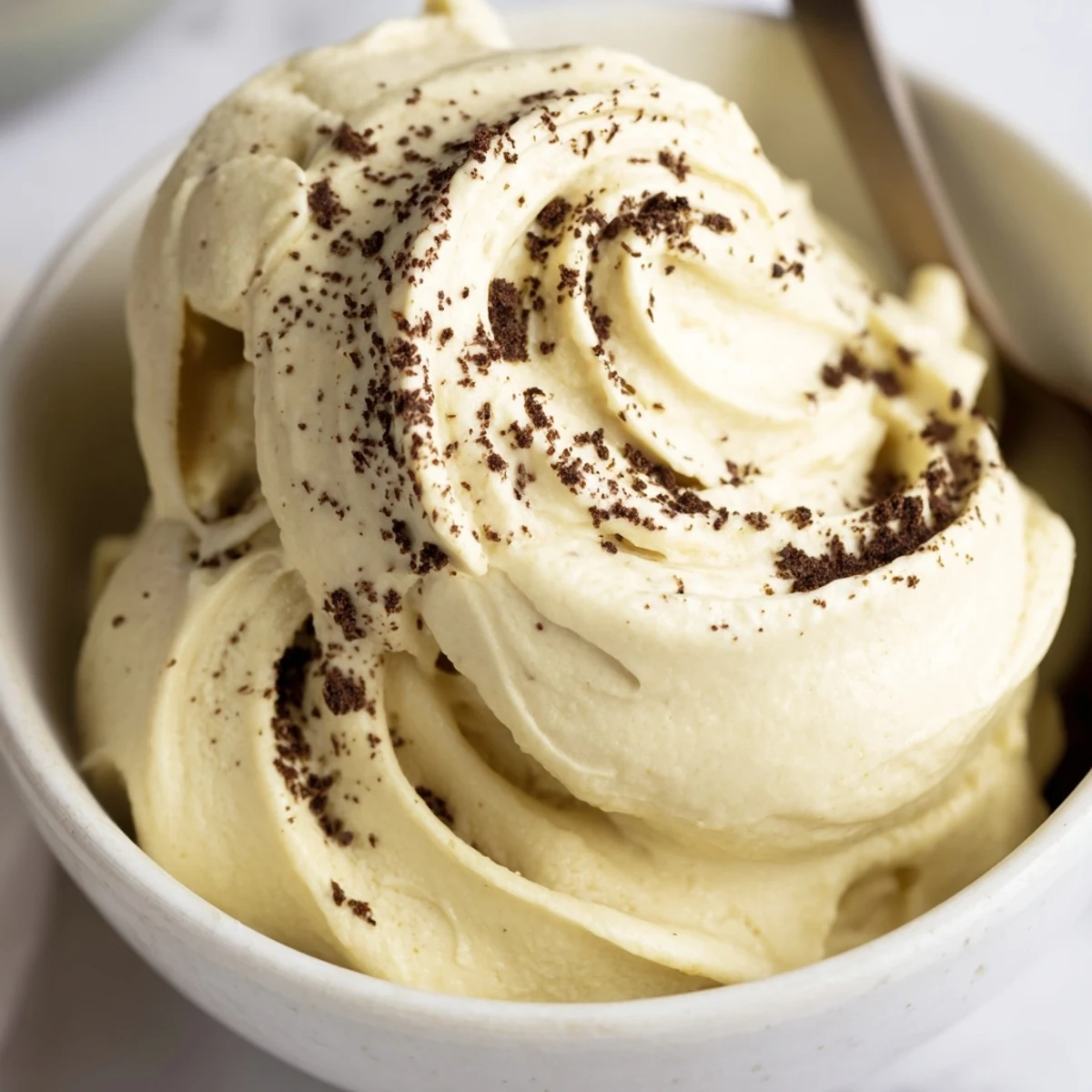Smooth soft serve banana nice cream in a white bowl garnished with dark chocolate chips and walnuts