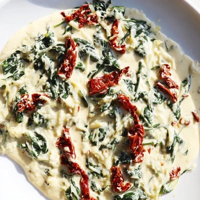 The rich Creamy Tuscan Garlic Sauce is served over fettuccine pasta in a white ceramic bowl.