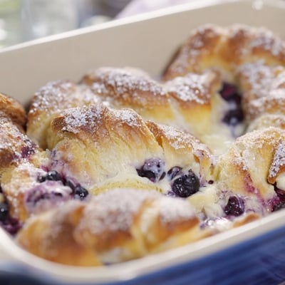 Slices of warm Blueberry Cream Cheese Croissant Casserole served on a white plate with a dusting of powdered sugar.